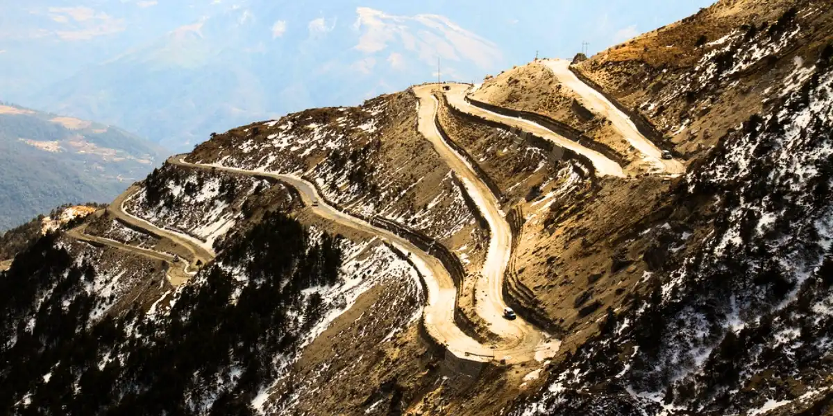 Winding mountain road through Sela Pass leading up to Tawang with prayer flags and rocky peaks
